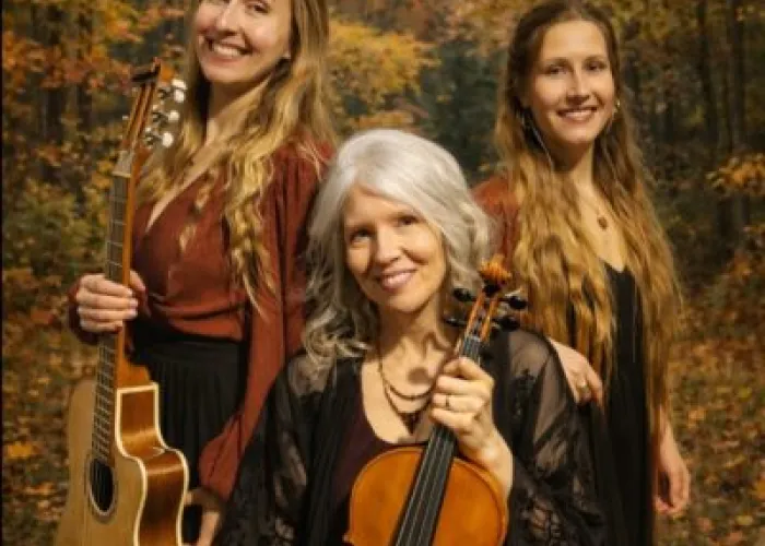 Three members of Mystikana pose together holding their instruments in a forest, autumn leaves on trees