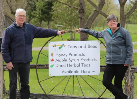 Photo of owners of teas and bees around their sign with wagon wheel in the background